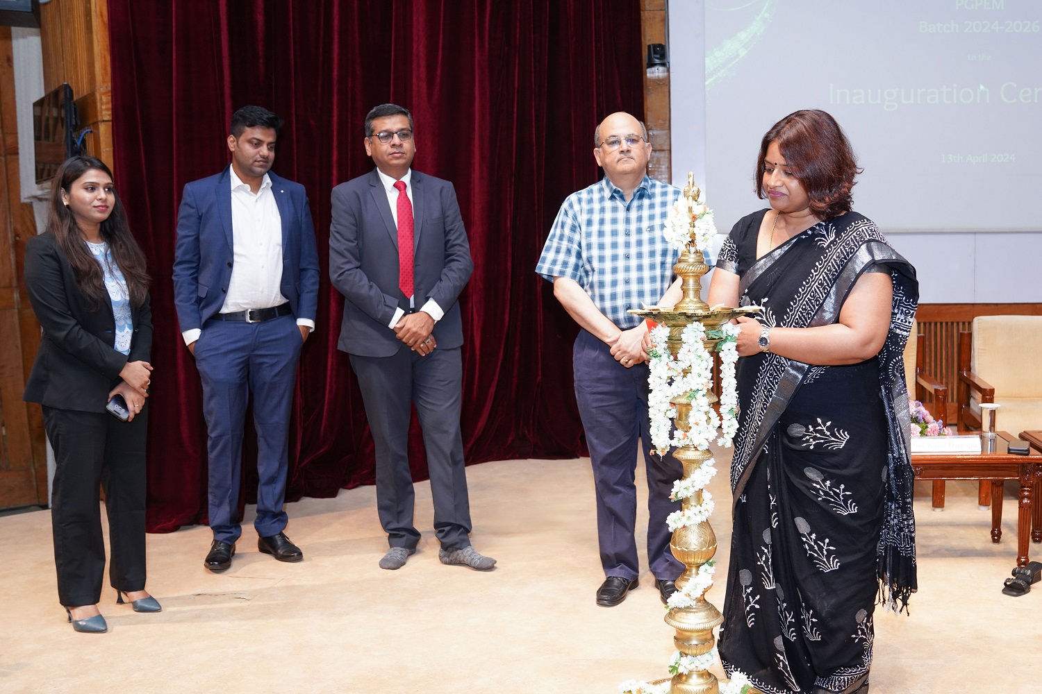 Chief Guests Mekhala Govinda, Services Director,  Dassault Systemes, lights the lamp at the inauguration of PGPEM Batch of  2024 – 2026. (L-R) representatives of the PGPEM batch of 2024-26, Chief Guest Jay Doshi Managing Director, Corporate Units, Digital, and India at BT Group, Prof. Rishikesha T Krishnan, Director, IIM Bangalore, looks on.